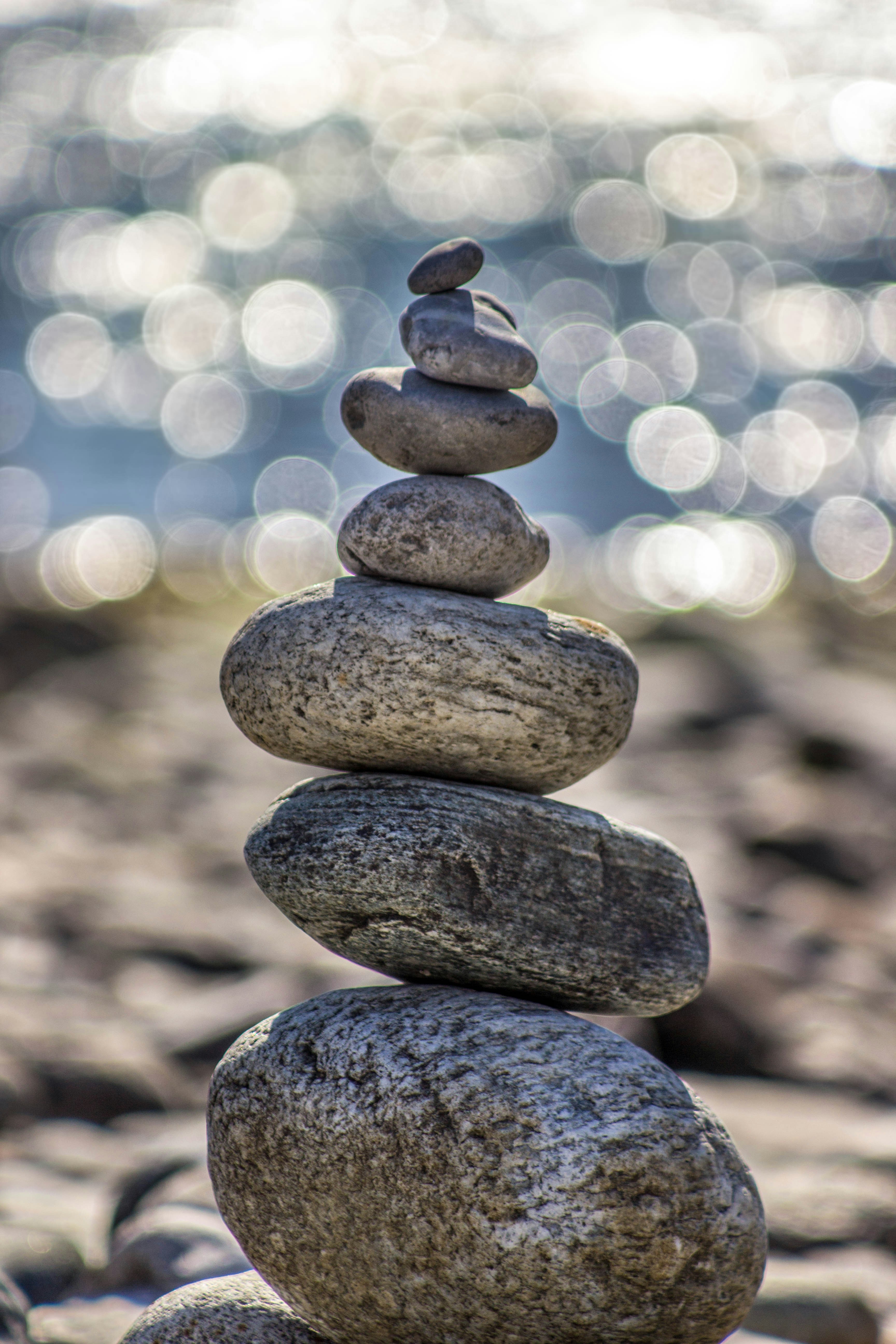 A stack of smooth stones balanced on top of each other near the ocean, symbolizing harmony, stability, and the transformative journey of life coaching.